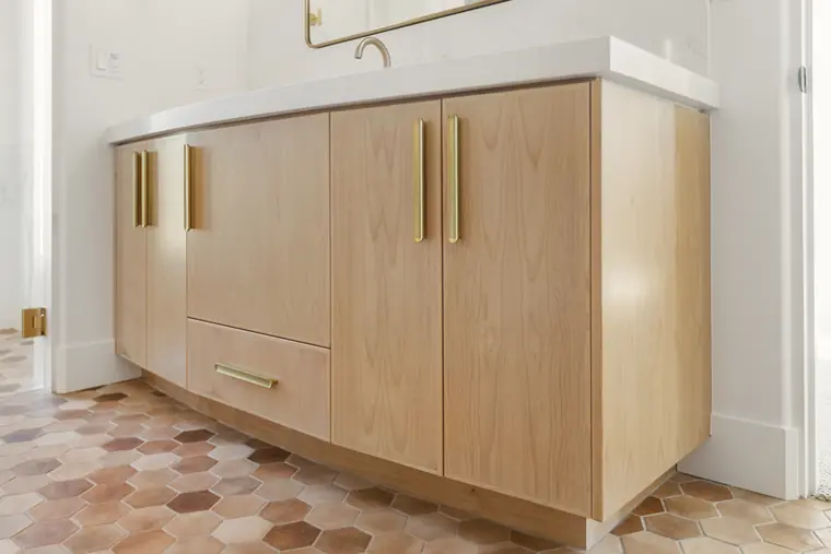 Wood vanity with brass pulls on terracotta hexagon tile