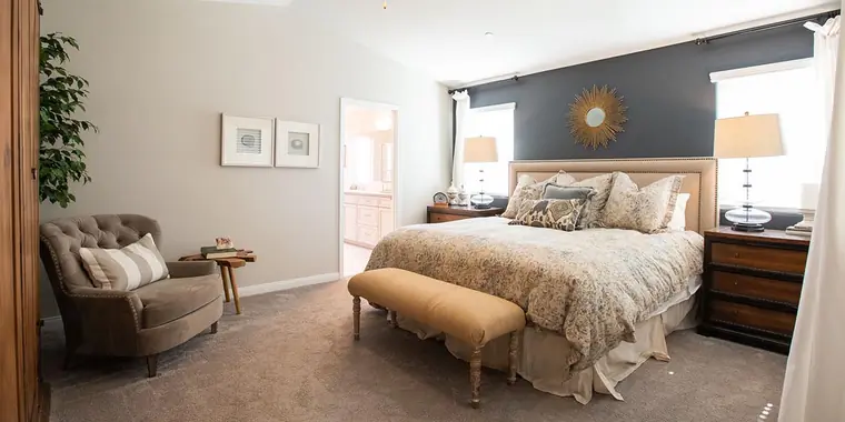 Primary bedroom with a gray accent wall and sitting chair