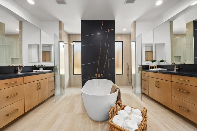 Primary bath with a freestanding tub, double wood vanities, and a dark stone wall