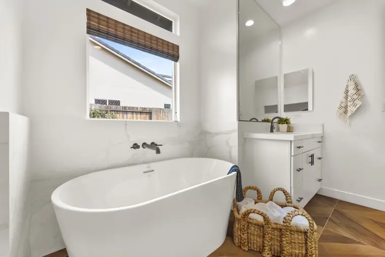 Freestanding tub under a window in a white primary bath