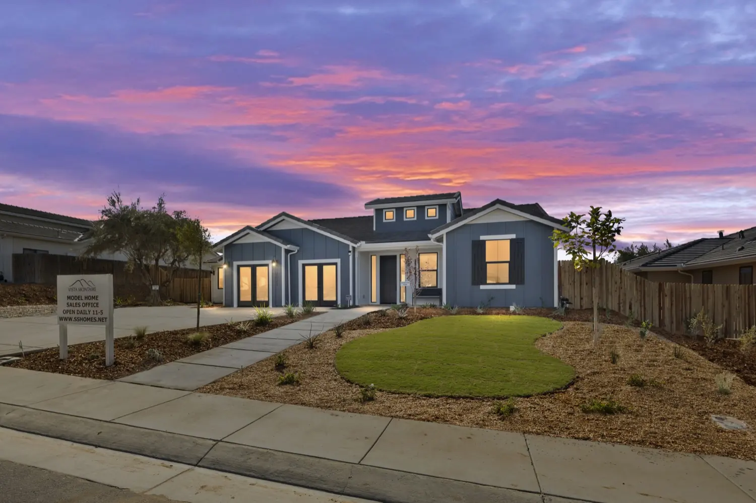 A farmhouse-style single-story model home at twilight with a front lawn