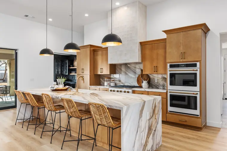 Kitchen with a marble waterfall island, wood cabinets, and dome pendants