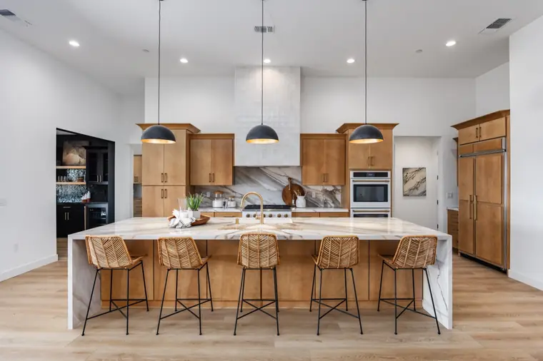 Kitchen island with woven counter stools under black pendants