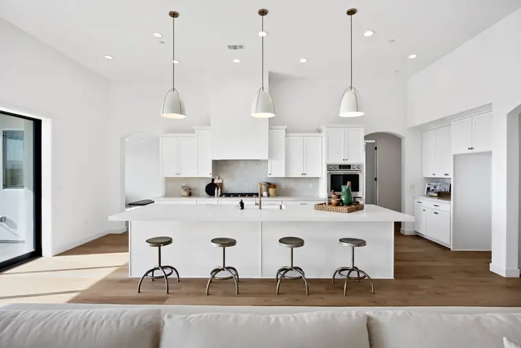 White kitchen with a large island, metal stools, and pendant lights