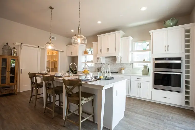 Kitchen island with bar seating, double wall ovens, and white cabinetry