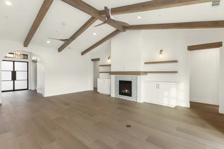 Beamed great room with a tiled fireplace and floating shelves