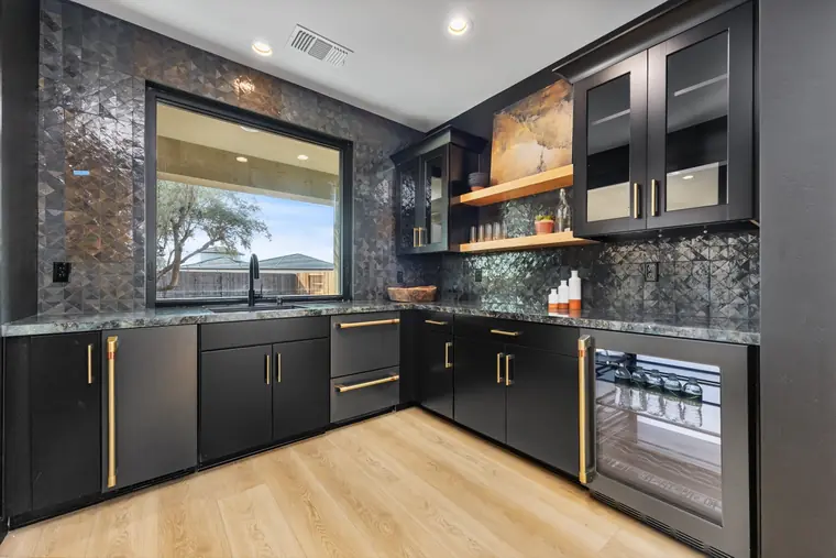 Wet bar with black cabinetry, gold hardware, and a window