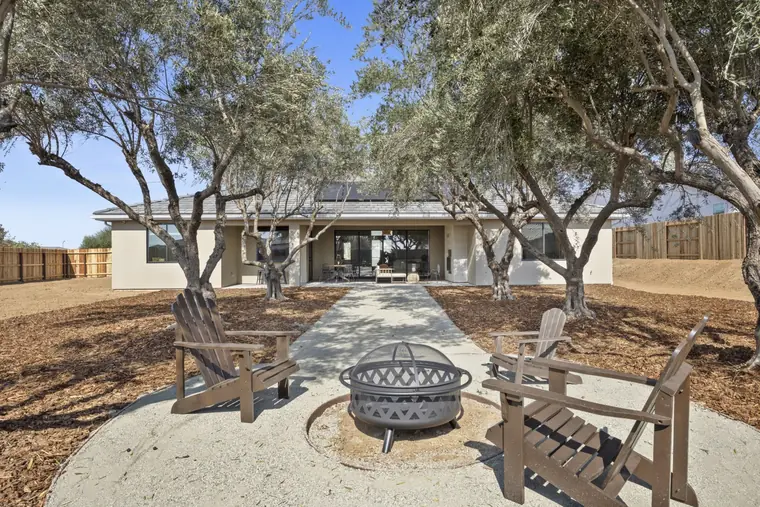 Backyard fire pit with Adirondack chairs under mature olive trees