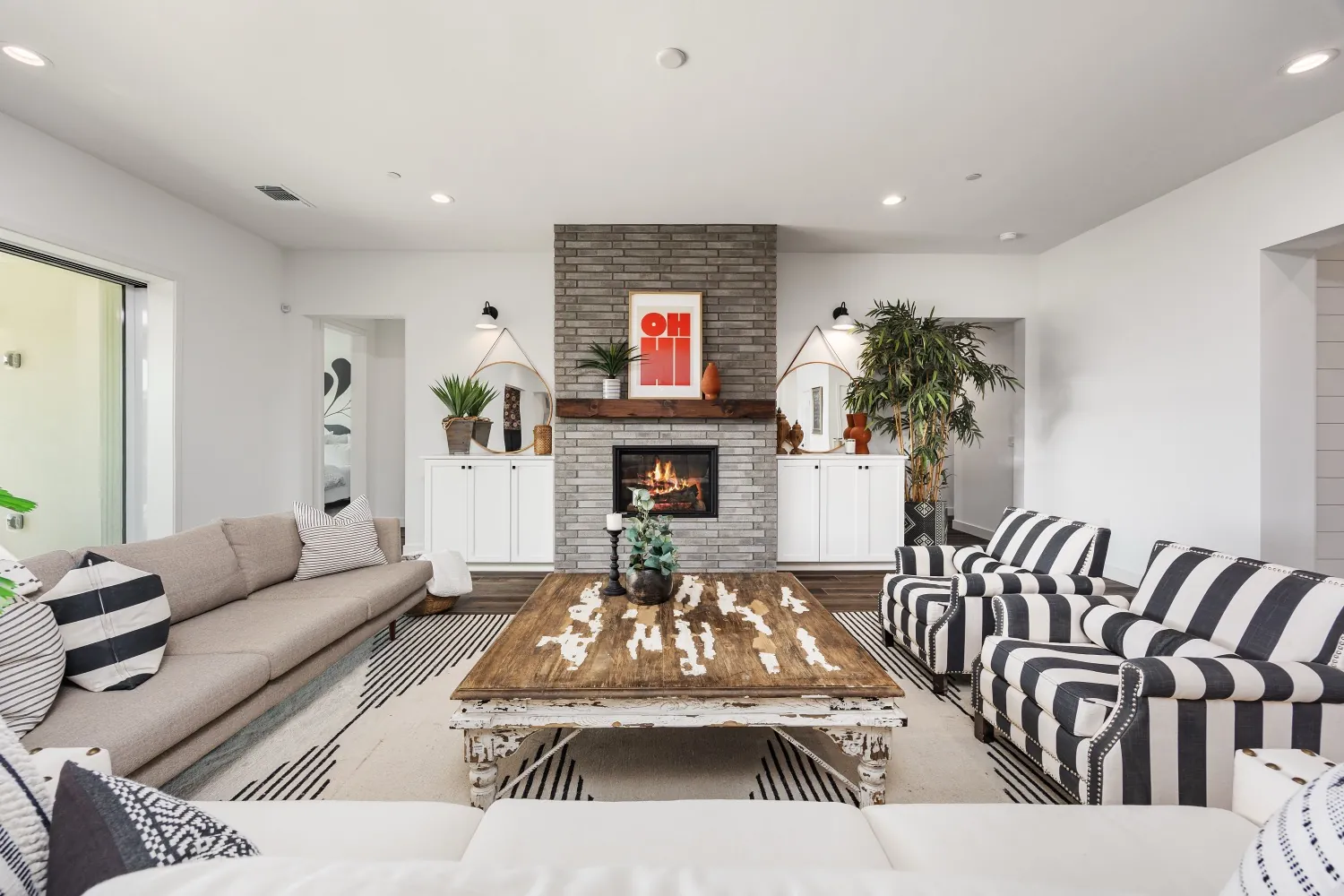Living room with a lit brick fireplace, striped armchairs, and wood floors