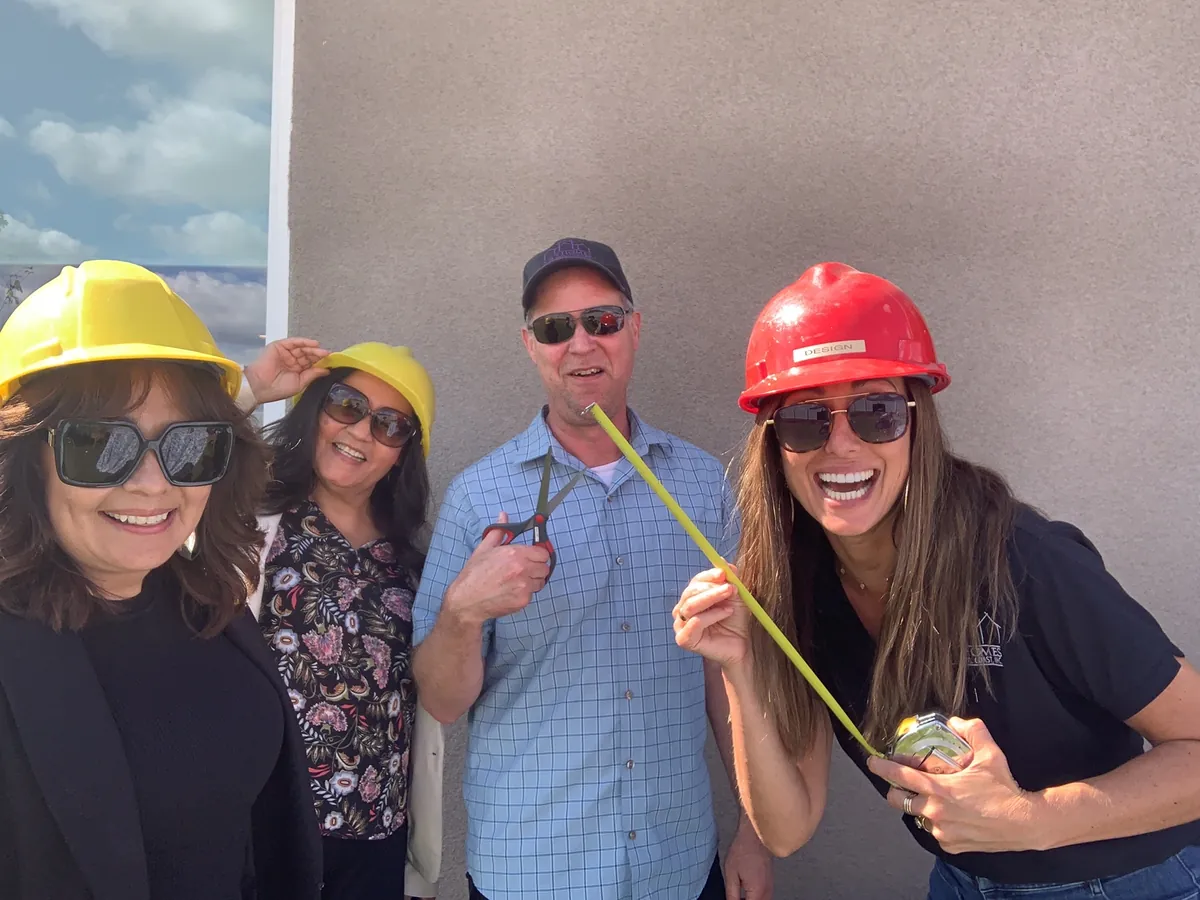 Four team members in hard hats laughing, one stretching a tape measure toward the camera