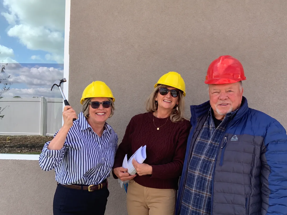 Janet, Warren, and Geri in hard hats, Janet holding up a hammer