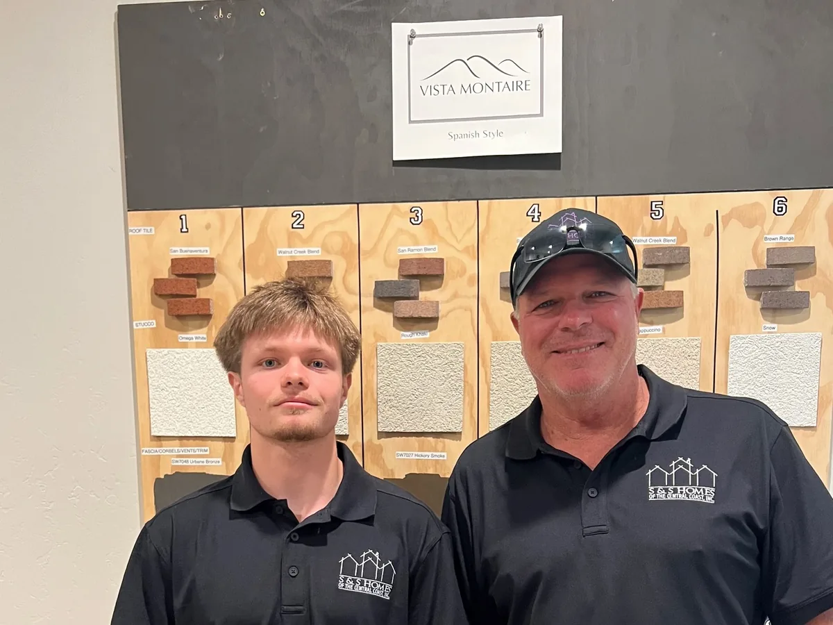 Steve Sanders and his son in black S&S Homes polos in front of a Vista Montaire Spanish-style finish board