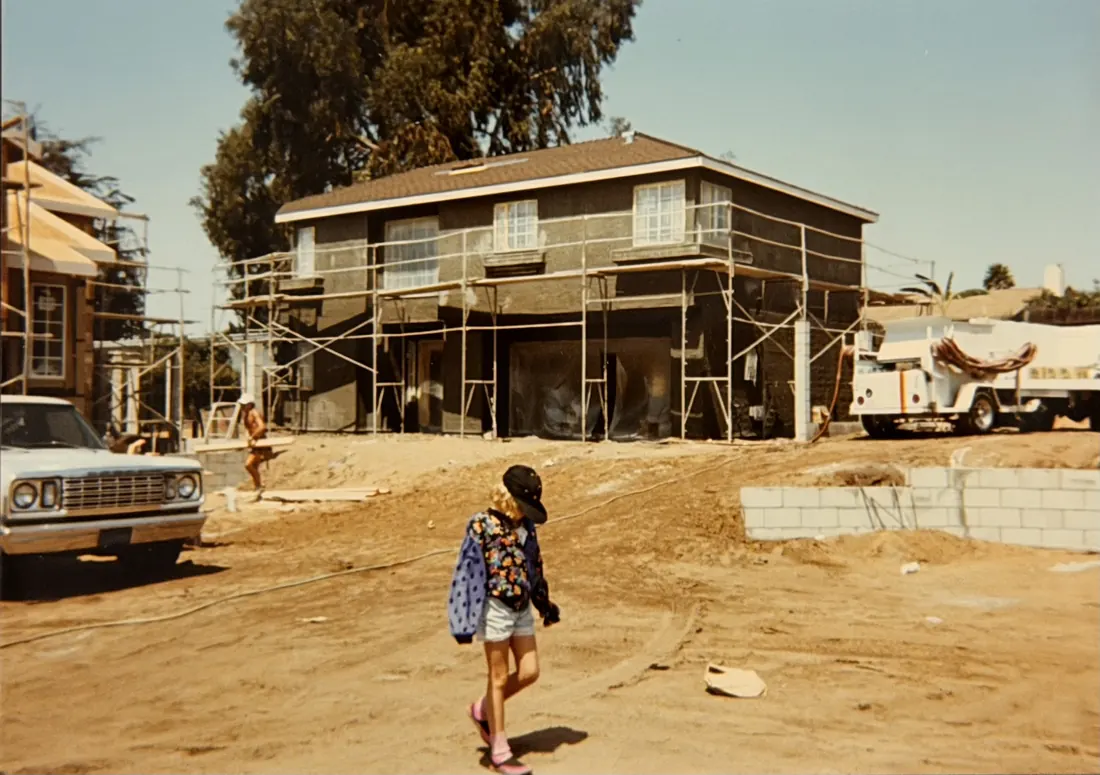 An early S&S home under construction, wrapped in scaffolding, with a child walking across the job site