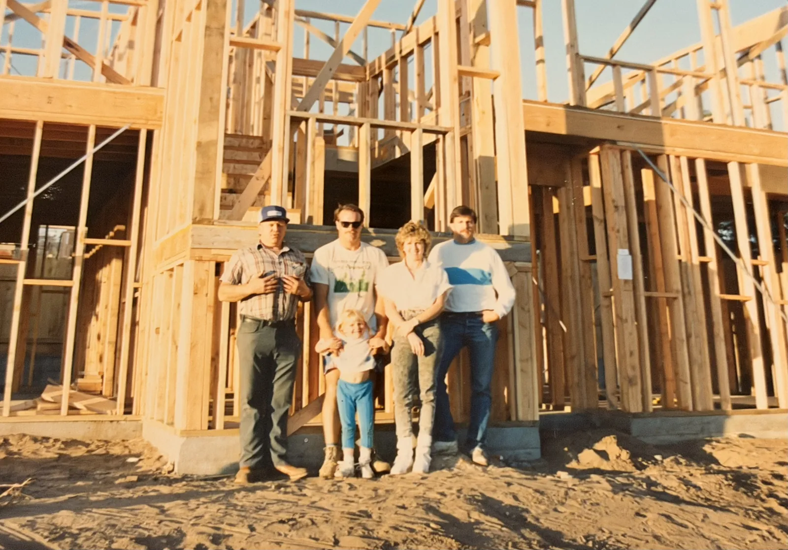 Five members of the Sanders family, four adults and a child, standing in front of a wood-framed house under construction